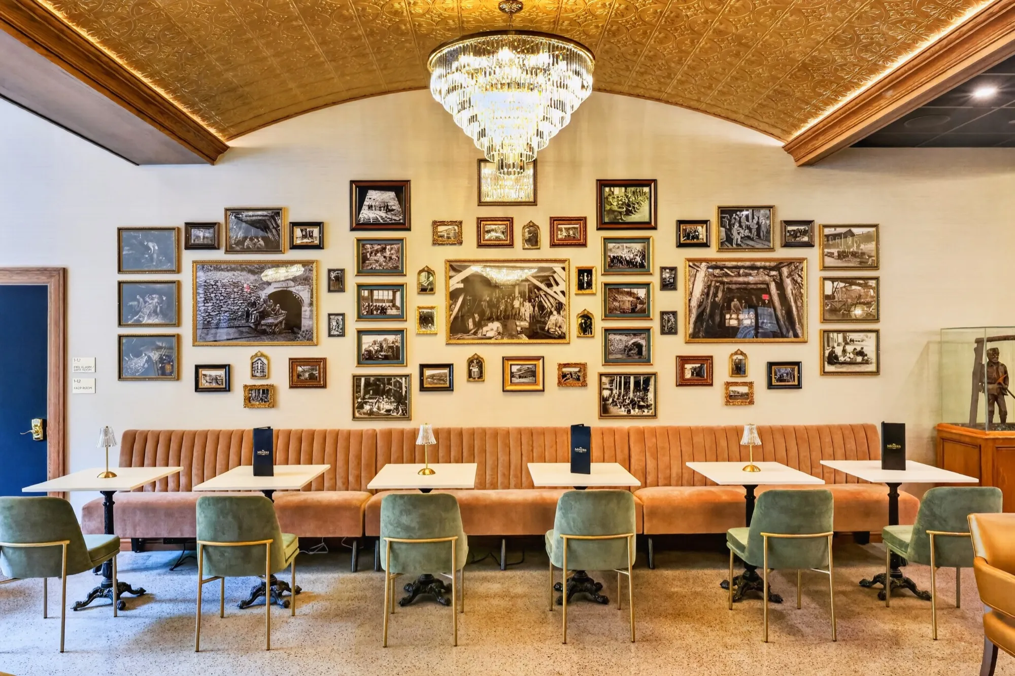 The Company Store Café, with velvet banquettes beneath the gilded vaulted ceiling and a wall of framed historic photographs