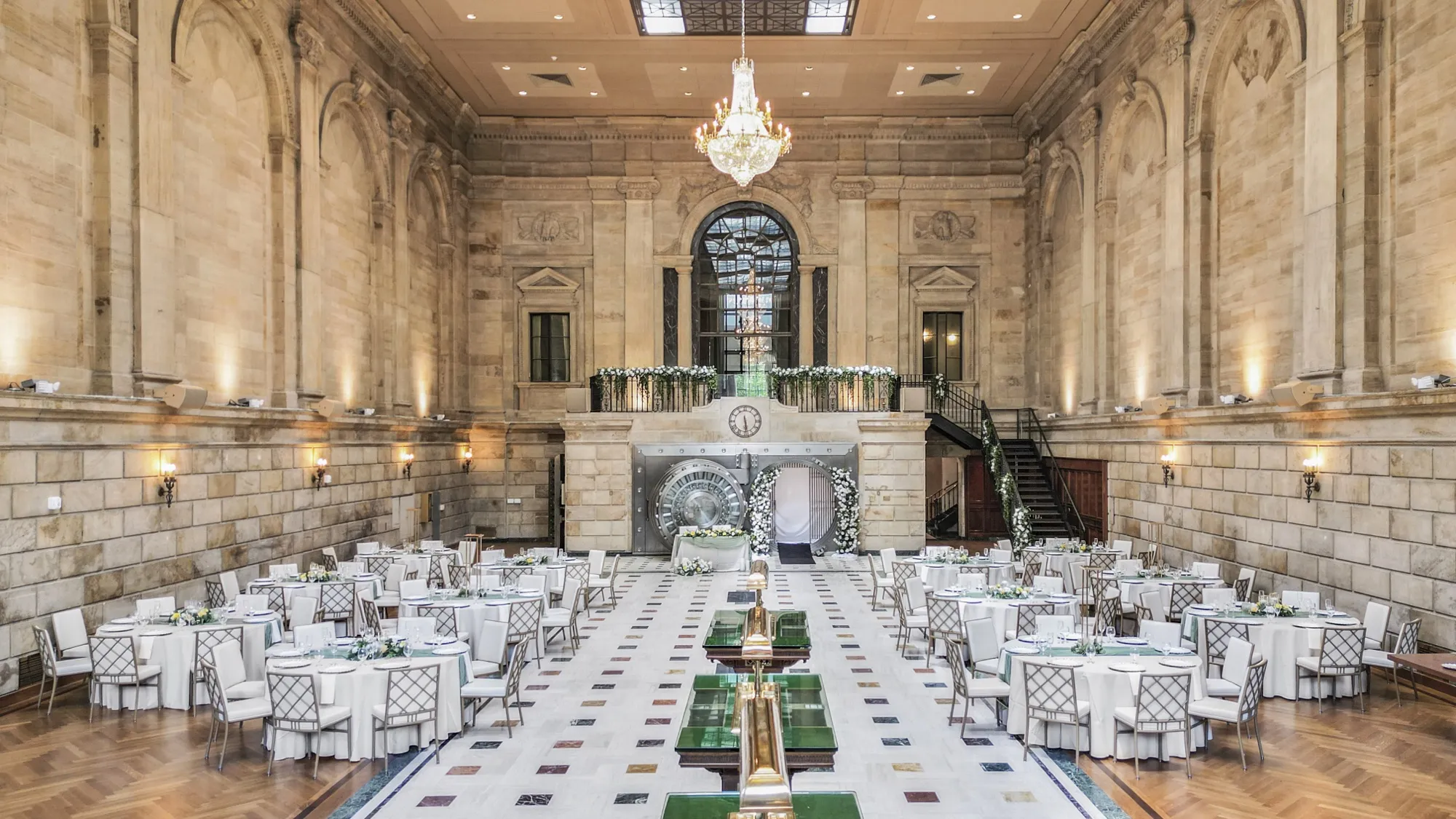 Wide-angle view of the grand banking hall at The Miners 1928, set with tables beneath the chandelier and stained-glass window