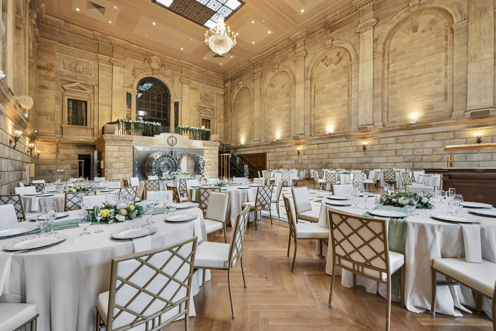 A wedding reception in the grand banking hall, set with round tables beneath the skylight and chandelier