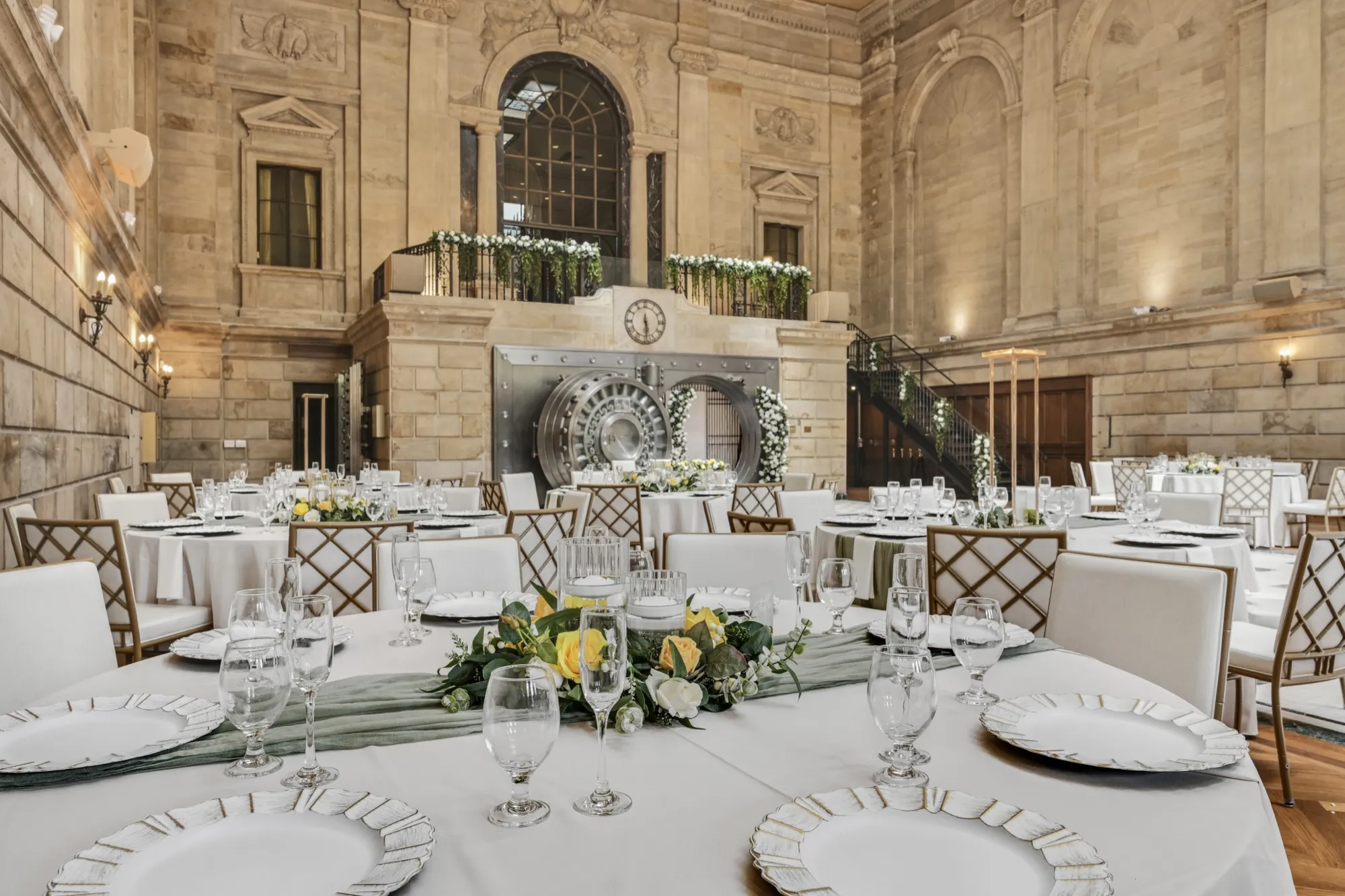 Reception tables set before the historic vault door beneath the balcony greenery