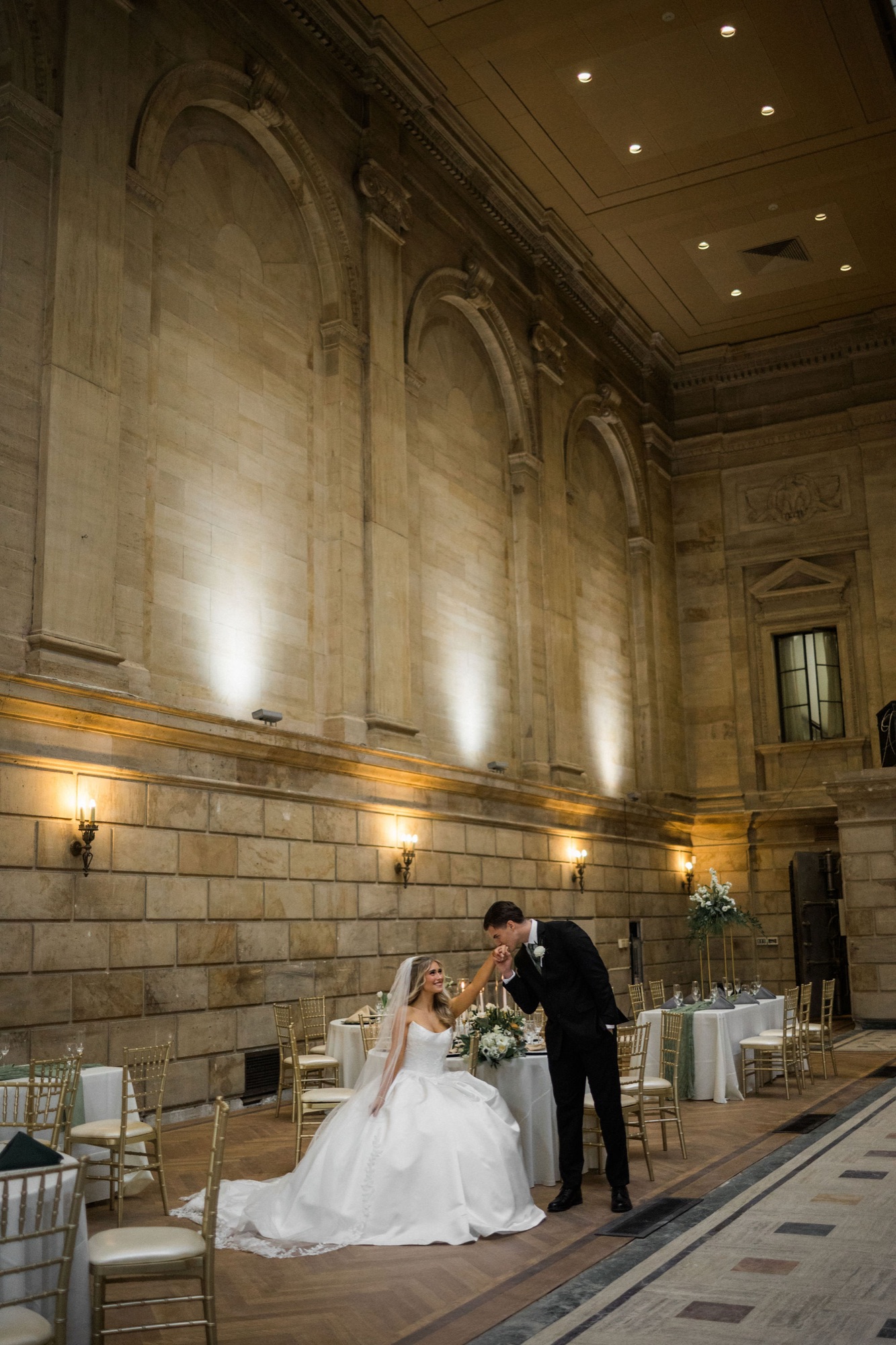 Bride and groom in the Bank Lobby, groom kissing the bride's hand under dramatic uplighting