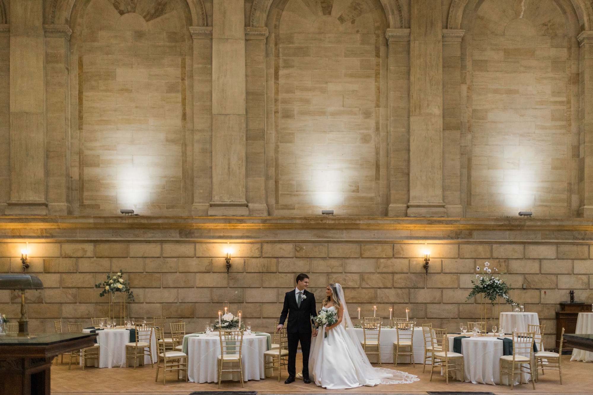 A couple standing in the Bank Lobby surrounded by limestone arches and elegantly set tables