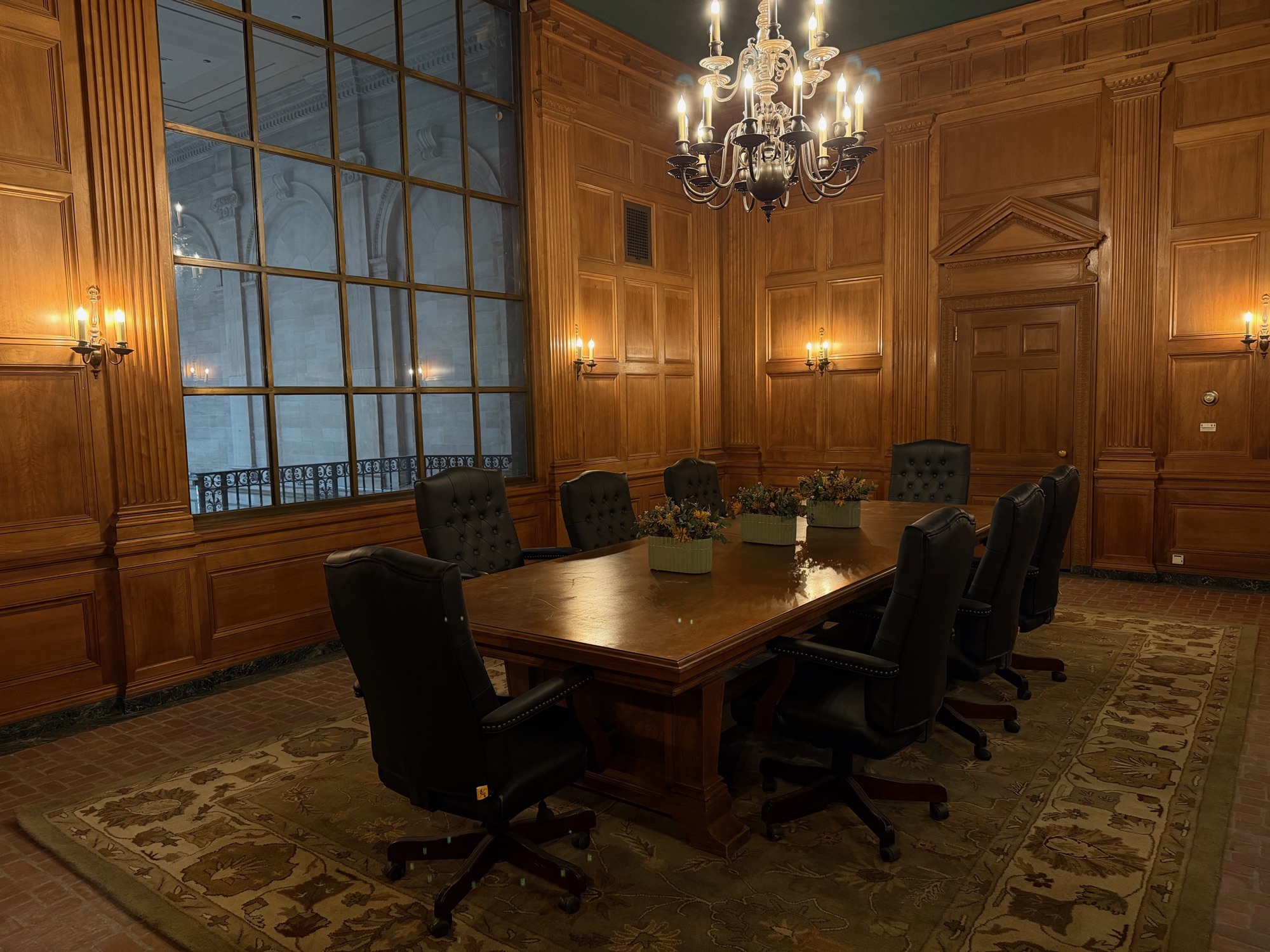 The Boardroom featuring rich wood paneling, chandelier, leather chairs, and window overlooking the Bank Lobby