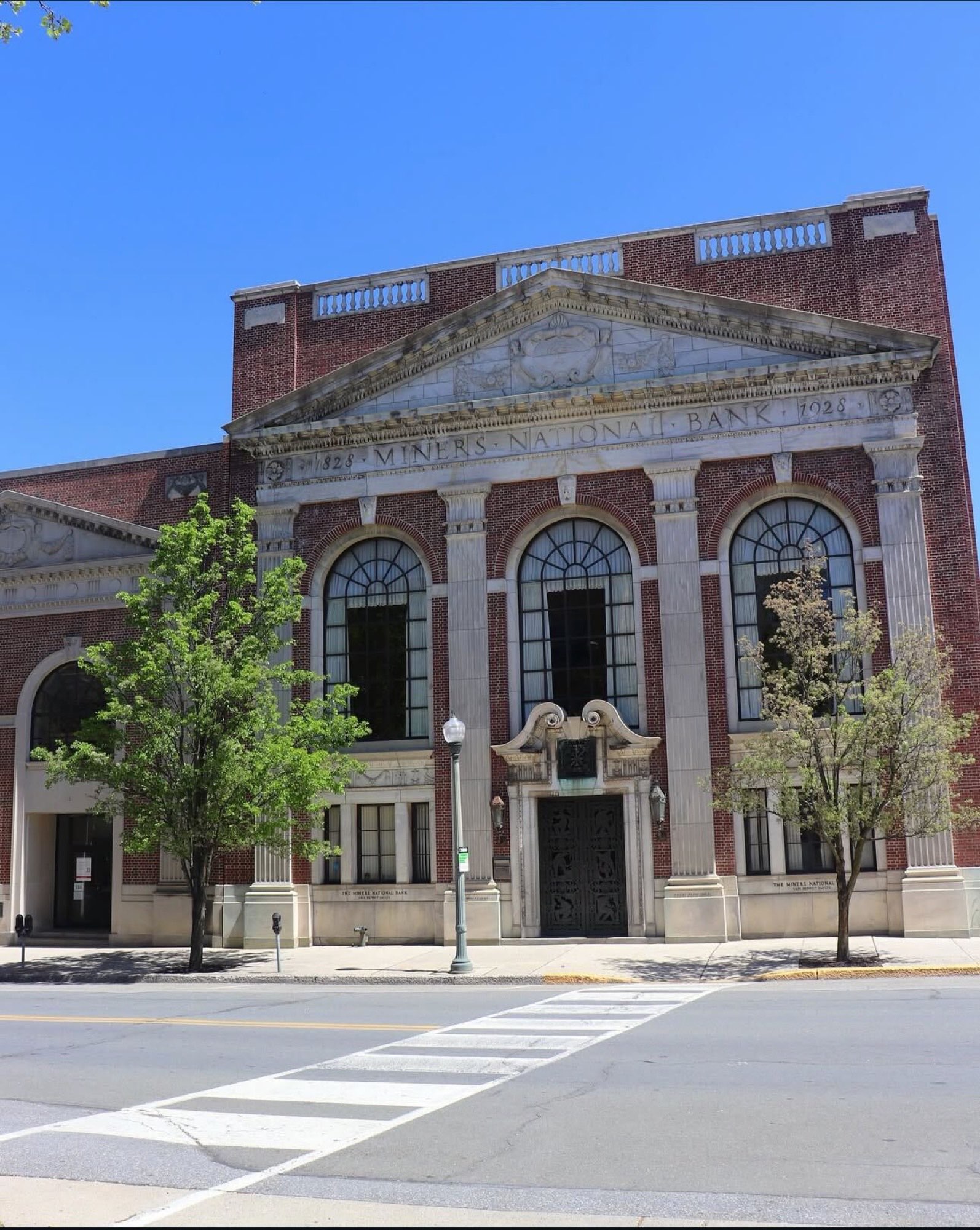 The neoclassical facade of The Miners 1928 featuring Harvard brick, Georgia marble Doric columns, three-story arched windows, and the original Miners National Bank pediment